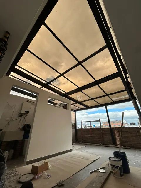 Marquesina en vidrio y estructura negra sobre terraza en proceso de obra — Bogotá