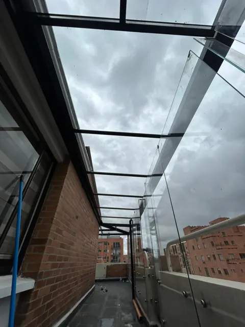 Marquesina en vidrio sobre corredor exterior entre muros en ladrillo — Bogotá