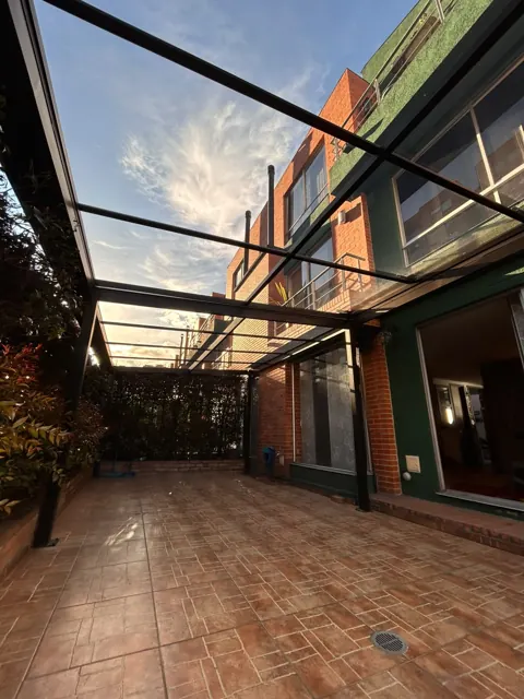 Marquesina en vidrio sobre patio con piso en baldosa y jardín — Bogotá