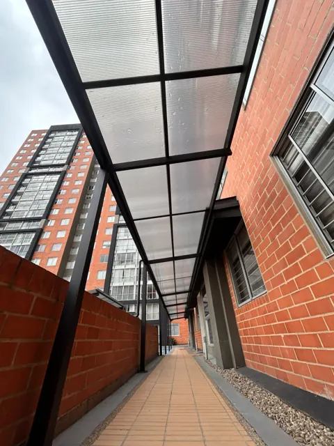Marquesina en policarbonato sobre corredor entre edificios en ladrillo — Bogotá